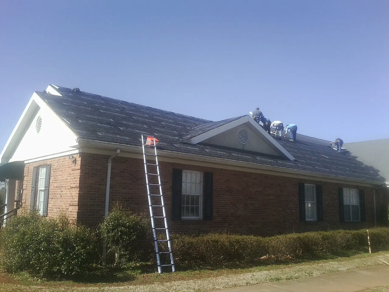 Crew tearing shingles off a brick ranch roof with a ladder set — Metal Roof Repair work by our crew in Alexander City