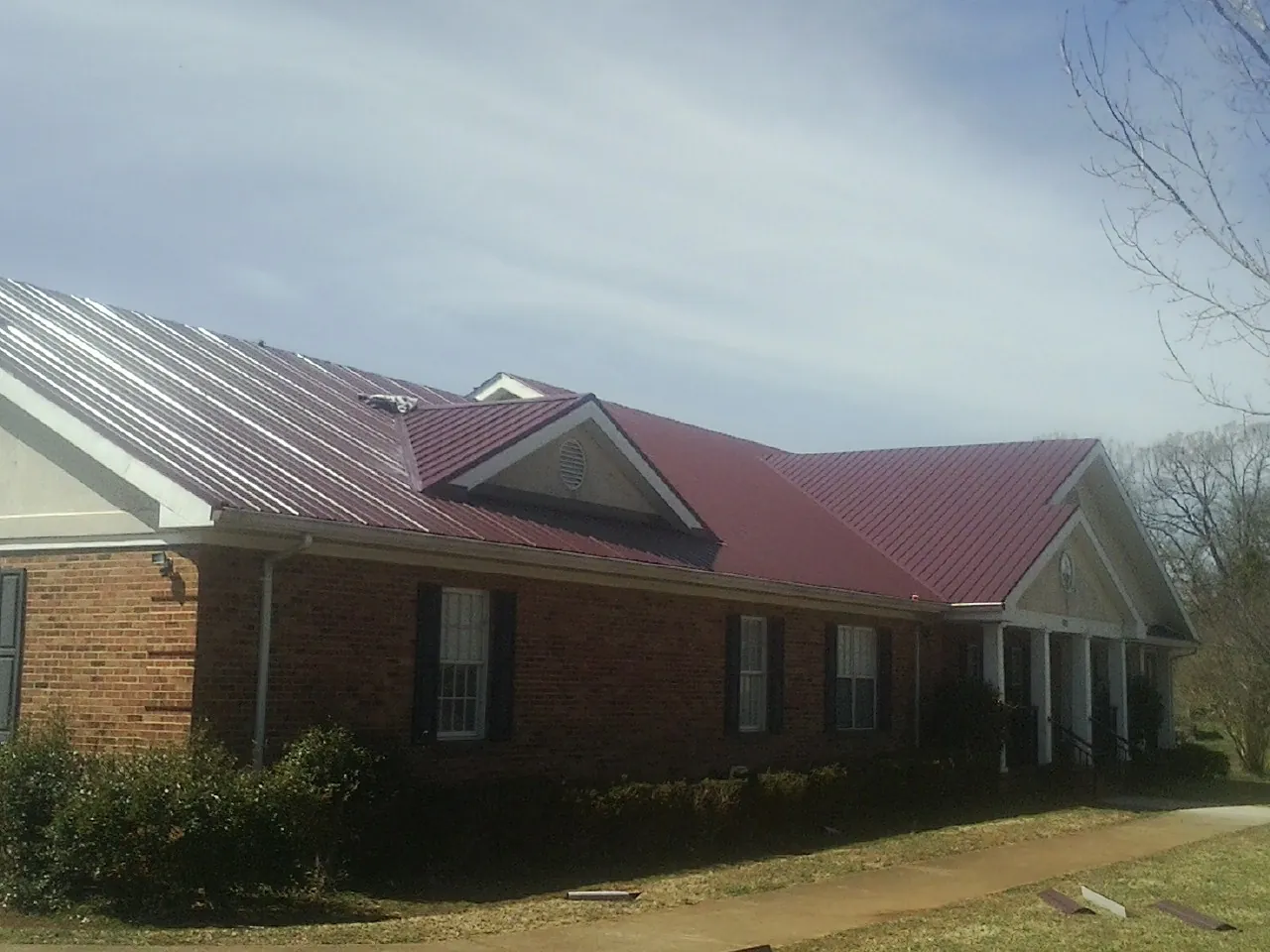 Red metal roof with gabled entries on a long brick building, from a Hail Damage Roof Repair job in Alexander City