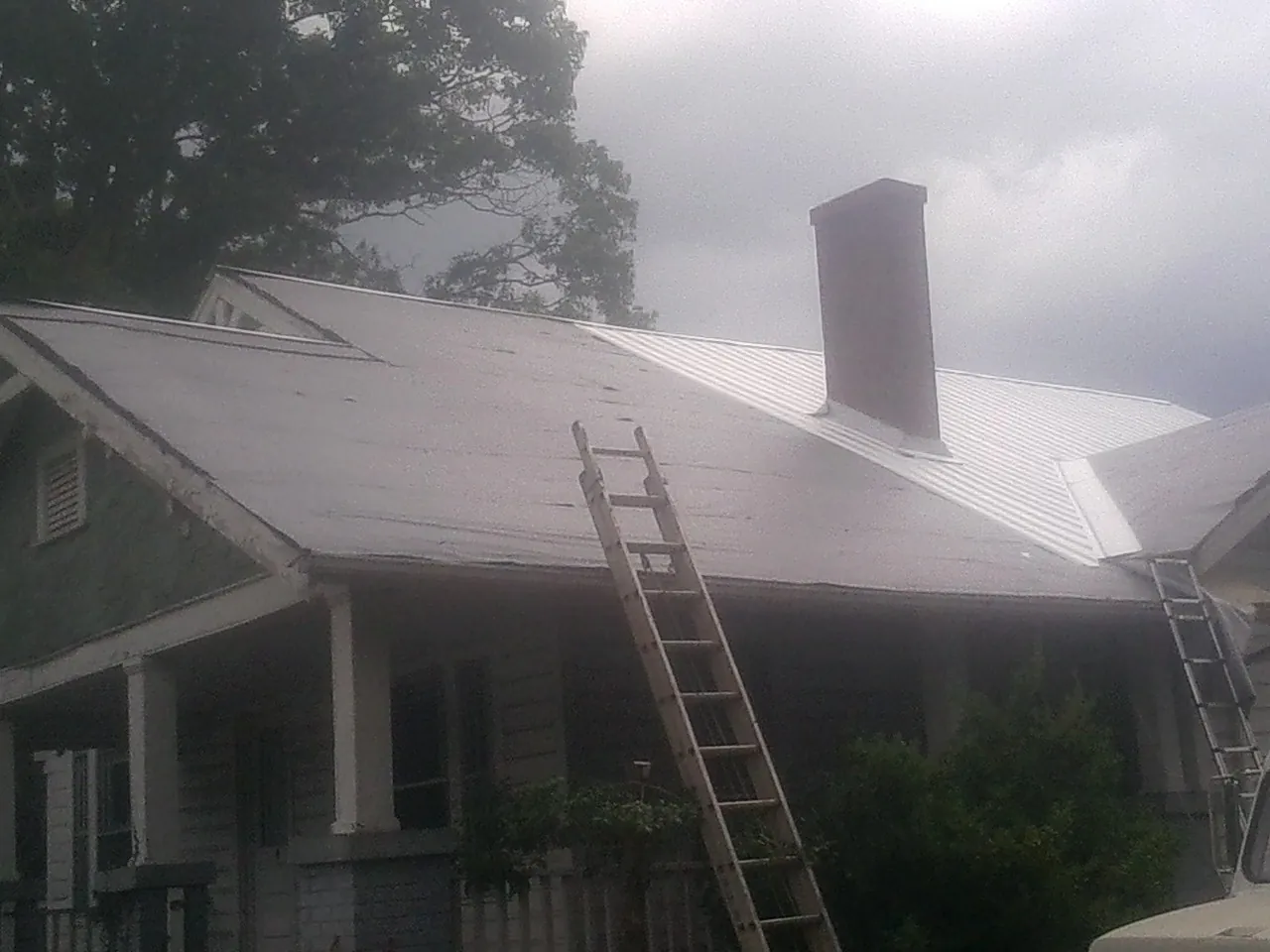 Ladders against a metal roof on an older home with a brick chimney in Alexander City
