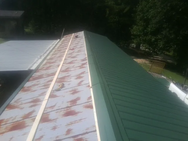 Old rusted panels beside newly installed green metal roofing — Wind Damage Roof Repair by Roofing Brothers in Alexander City