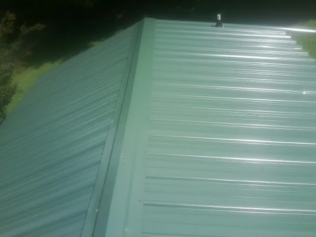 New green metal panels meeting at the ridge of a roof — Flat Roof Repair work by our crew in Alexander City