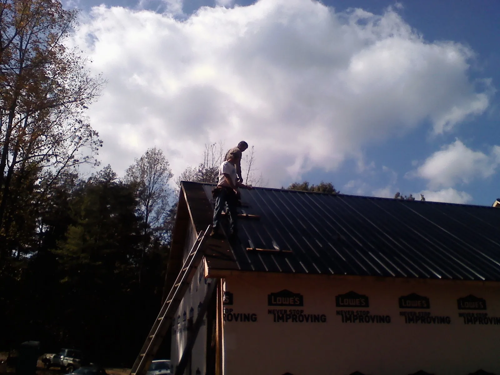 Roofer fastening dark metal panels high against a cloudy sky, from a Roof Inspection job in Alexander City