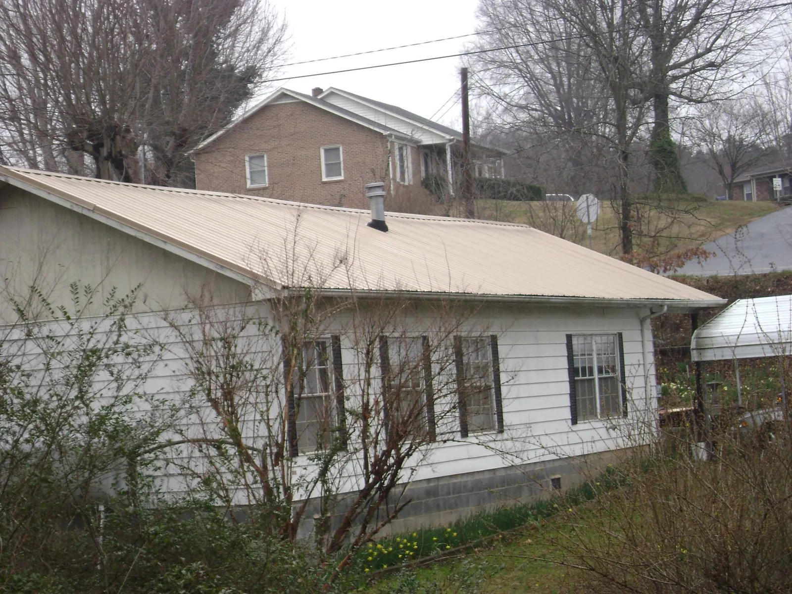 Tan metal roof on a white sided house set into a hillside — Commercial Roofing by Roofing Brothers in Alexander City