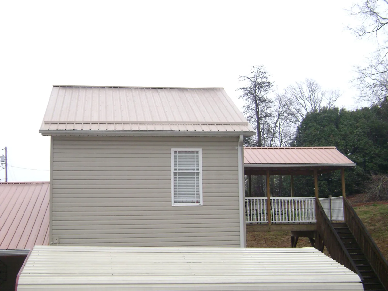 Tan metal roofs on a two story addition and attached porch, from a Roof Replacement job in Alexander City
